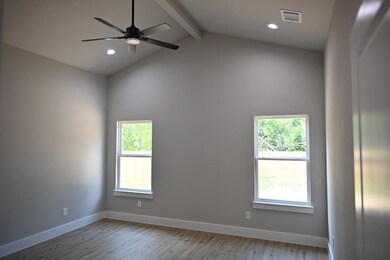 Unfurnished room featuring wood-type flooring, vaulted ceiling with beams, ceiling fan, and a wealth of natural light