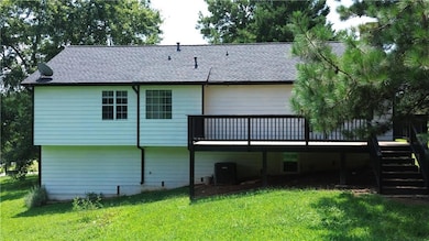 Back of property featuring a deck, roof with shingles, stairs, and a lawn