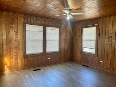Unfurnished room featuring wooden ceiling, a ceiling fan, hardwood / wood-style floors, and wooden walls