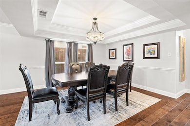 Dining area featuring a raised ceiling, dark wood-type flooring, a chandelier, and crown molding
