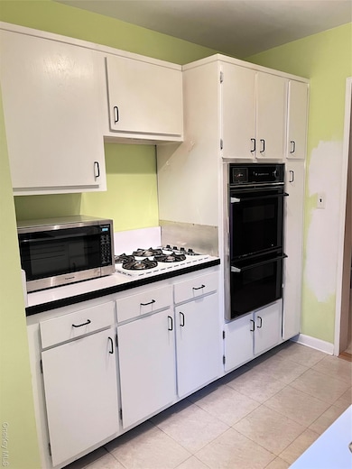 Kitchen featuring white cabinetry, light tile patterned floors, double oven, and stovetop