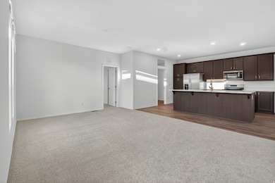 Kitchen featuring dark carpet, open floor plan, stainless steel appliances, a kitchen bar, and a kitchen island with sink