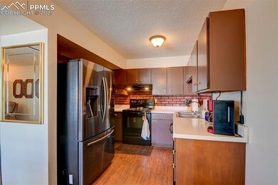 Kitchen featuring stainless steel fridge, black / electric stove, under cabinet range hood, light countertops, and a textured ceiling