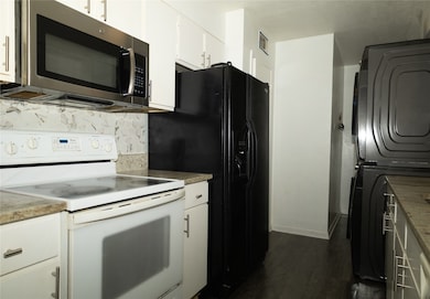 Kitchen with white range with electric cooktop, stainless steel microwave, dark wood-style floors, tasteful backsplash, and white cabinets