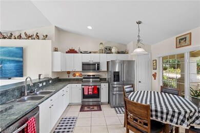 Kitchen with vaulted ceiling, light tile patterned flooring, stainless steel appliances, white cabinetry, and pendant lighting