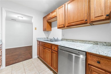 Kitchen featuring stainless steel dishwasher, a sink, light tile patterned floors, and light stone counters