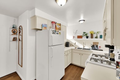 Kitchen featuring white appliances, dark wood-style flooring, light countertops, and open shelves