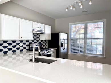 Kitchen featuring tasteful backsplash, light stone counters, appliances with stainless steel finishes, white cabinets, and under cabinet range hood