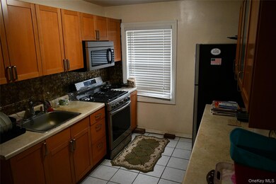 Kitchen featuring stainless steel appliances, brown cabinetry, light countertops, light tile patterned floors, and backsplash