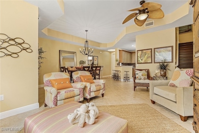 Living area with ceiling fan with notable chandelier, light tile patterned flooring, visible vents, a tray ceiling, and baseboards