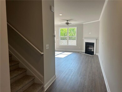 Unfurnished living room with wood finished floors, a glass covered fireplace, crown molding, a ceiling fan, and stairway