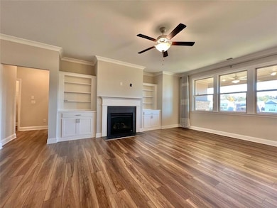 Unfurnished living room with ornamental molding, ceiling fan, built in features, dark wood-type flooring, and a fireplace