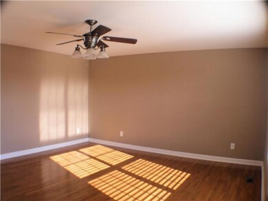 Great room has hardwood floors, ceiling fan, and large windows.