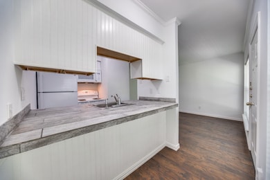 Kitchen featuring white appliances, dark wood-type flooring, white cabinetry, crown molding, and tile countertops
