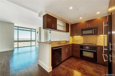 Kitchen featuring a wall of windows, decorative backsplash, black appliances, light stone counters, and dark wood-style flooring