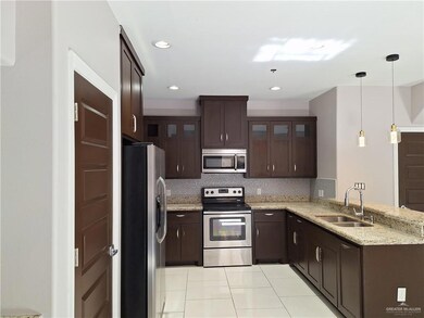 Kitchen featuring backsplash, appliances with stainless steel finishes, light stone counters, light tile patterned floors, and sink