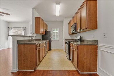 Kitchen with stainless steel appliances, a ceiling fan, brown cabinetry, dark countertops, and a sink
