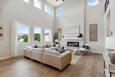 Living room featuring a towering ceiling, a glass covered fireplace, light wood-type flooring, and ceiling fan