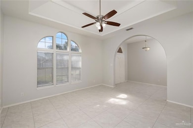 Spare room with a tray ceiling, ceiling fan, light tile patterned floors, and arched walkways