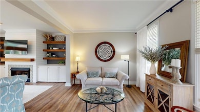 Living area featuring a fireplace, wood finished floors, baseboards, and ornamental molding