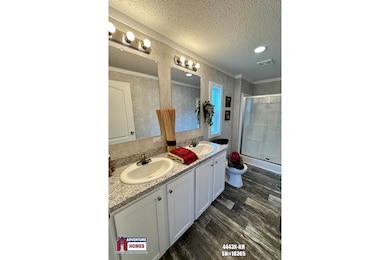 bathroom featuring a textured ceiling, a shower with door, double vanity, ornamental molding, and wood finished floors