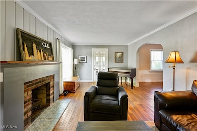 Living room with crown molding, arched walkways, wood-type flooring, a fireplace, and a textured ceiling