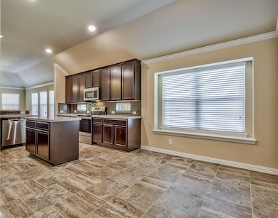 Kitchen with appliances with stainless steel finishes, backsplash, lofted ceiling, a center island, and light tile floors