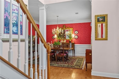 Foyer entrance with wood finished floors, ornamental molding, a wainscoted wall, a chandelier, and stairs