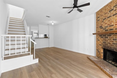 Unfurnished living room featuring stairway, light wood-type flooring, a brick fireplace, and ceiling fan