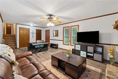 Living area featuring stairs, light wood-style flooring, ceiling fan, baseboards, and ornamental molding