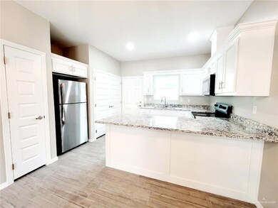 Kitchen featuring stainless steel appliances, a peninsula, light stone countertops, white cabinetry, and recessed lighting