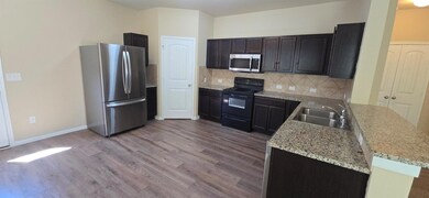 Kitchen with stainless steel appliances, decorative backsplash, dark wood finished floors, light stone counters, and a peninsula