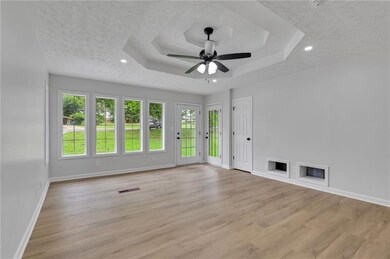 Spare room with a textured ceiling, baseboards, a raised ceiling, light wood-type flooring, and a ceiling fan