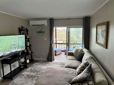 Living area with a textured ceiling, wooden walls, ornamental molding, a wall mounted AC, and wood finished floors