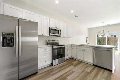 Kitchen with stainless steel appliances, white cabinets, hanging light fixtures, light wood-style flooring, and a peninsula