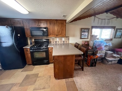 Kitchen with a peninsula, light countertops, brown cabinets, black appliances, and a kitchen bar