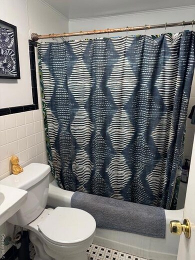 Bathroom with tile walls, shower / bath combination with curtain, tile patterned floors, and crown molding