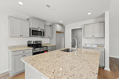 Kitchen with gray cabinets, stainless steel appliances, light stone counters, light wood finished floors, and recessed lighting