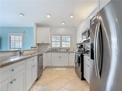 Kitchen featuring appliances with stainless steel finishes, a sink, white cabinetry, light stone counters, and light tile patterned flooring