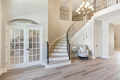The curved staircase creates a grand focal point, complemented by a set of graceful French doors leading into a private room. Wide-plank flooring and soft natural light give this space a warm, welcoming feel.