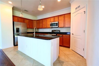 Kitchen with appliances with stainless steel finishes, dark countertops, ornamental molding, light tile patterned flooring, and decorative light fixtures