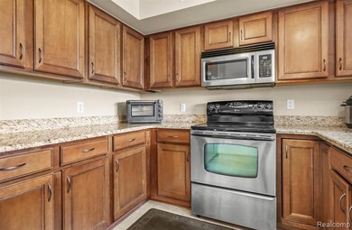 Kitchen with brown cabinetry, stainless steel appliances, light stone counters, and light tile patterned floors