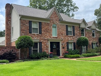 View of front of property featuring a chimney, a front yard, brick siding, and roof with shingles