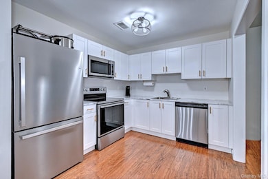 Kitchen with stainless steel appliances, white cabinetry, and light wood-style flooring
