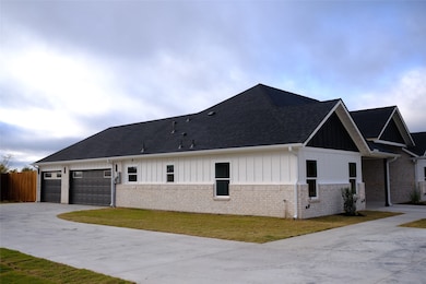 View of side of property with board and batten siding, concrete driveway, a garage, a yard, and brick siding
