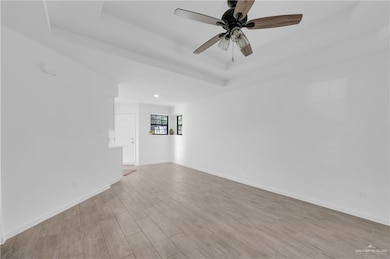 Spare room featuring a raised ceiling, light wood-style floors, and ceiling fan