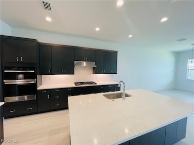 Kitchen featuring dark cabinets, recessed lighting, tasteful backsplash, light stone counters, and appliances with stainless steel finishes