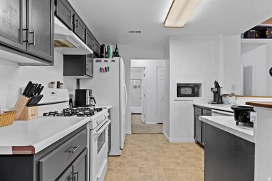 Kitchen with white appliances, light countertops, under cabinet range hood, gray cabinets, and dark cabinetry