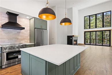 Kitchen with green cabinets, premium appliances, wall chimney range hood, decorative backsplash, and light wood finished floors