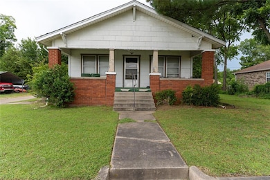 Bungalow-style house featuring covered porch, a front lawn, brick siding, and a carport